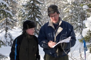 En man och en pojke tittar på en karta i den snöiga skogen.