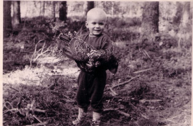Mustavalkoinen valokuva, jossa pikkupoika lintu käsissään.