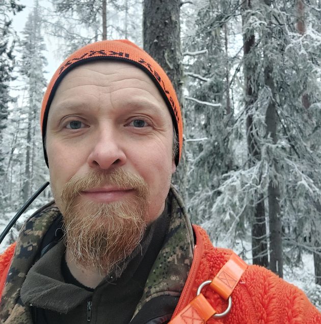 Mies katsoo kameraan talvisessa metsässä.