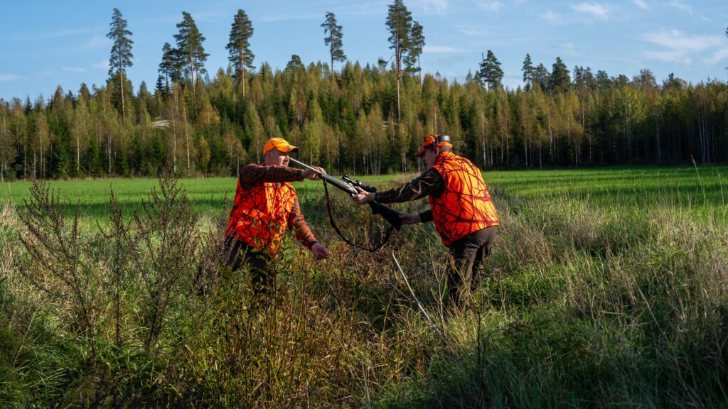 Metsästäjä ojentaa toiselle kiväärinsä.